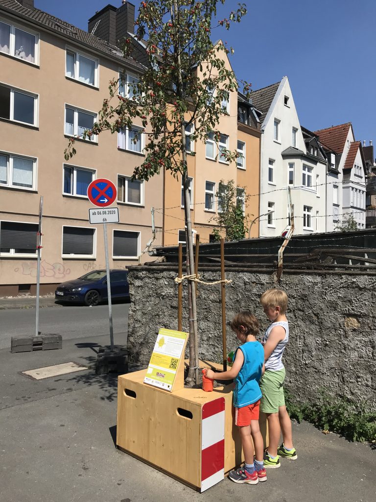 Sommerliche Hitze: Kinder gießen einen Wanderbaum in der Kleinen Gildenstraße in Hörde